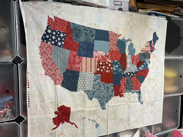 Fabric art of the United States map featuring various patriotic patterns in red, white, and blue, including stars and stripes.