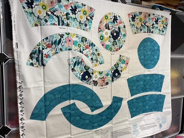 A layout of sewing pattern pieces on fabric, featuring floral designs in various colors and solid teal sections for garment construction.