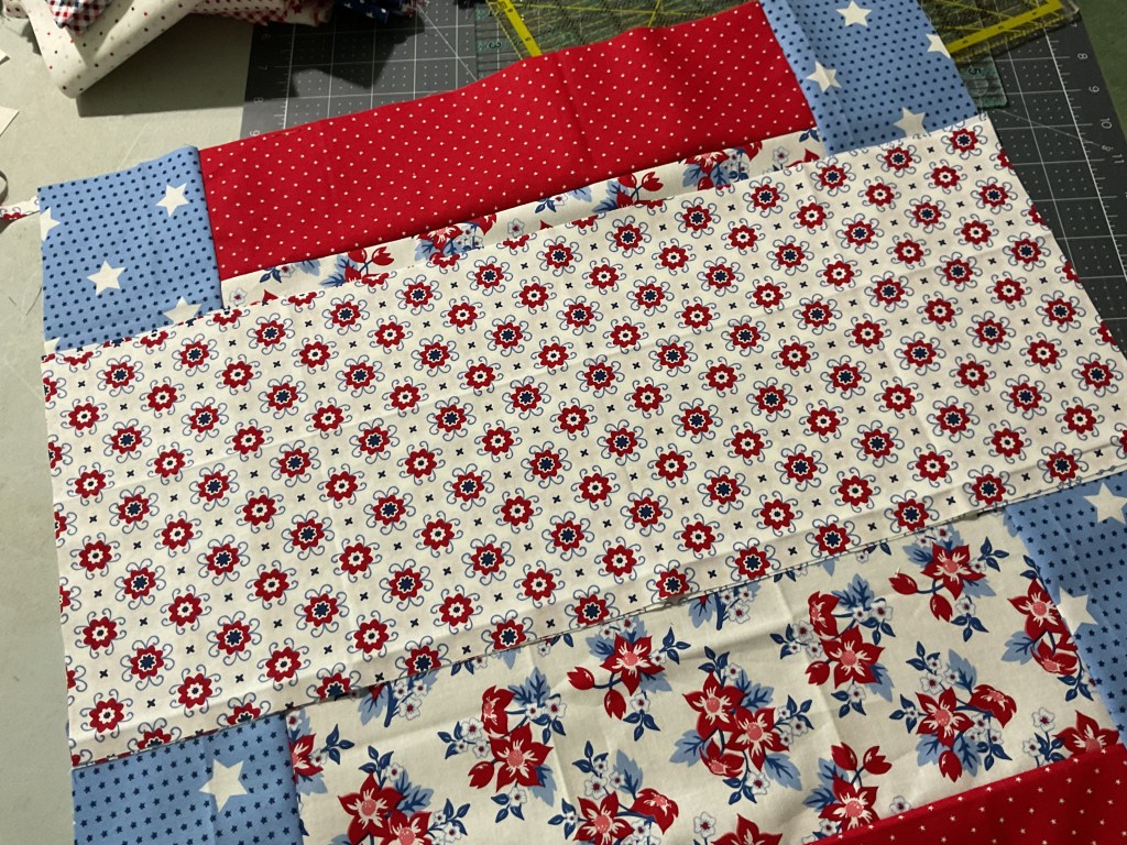 A patchwork of colorful fabrics, including red, blue, and white patterns, showcasing floral designs and polka dots arranged on a cutting mat.