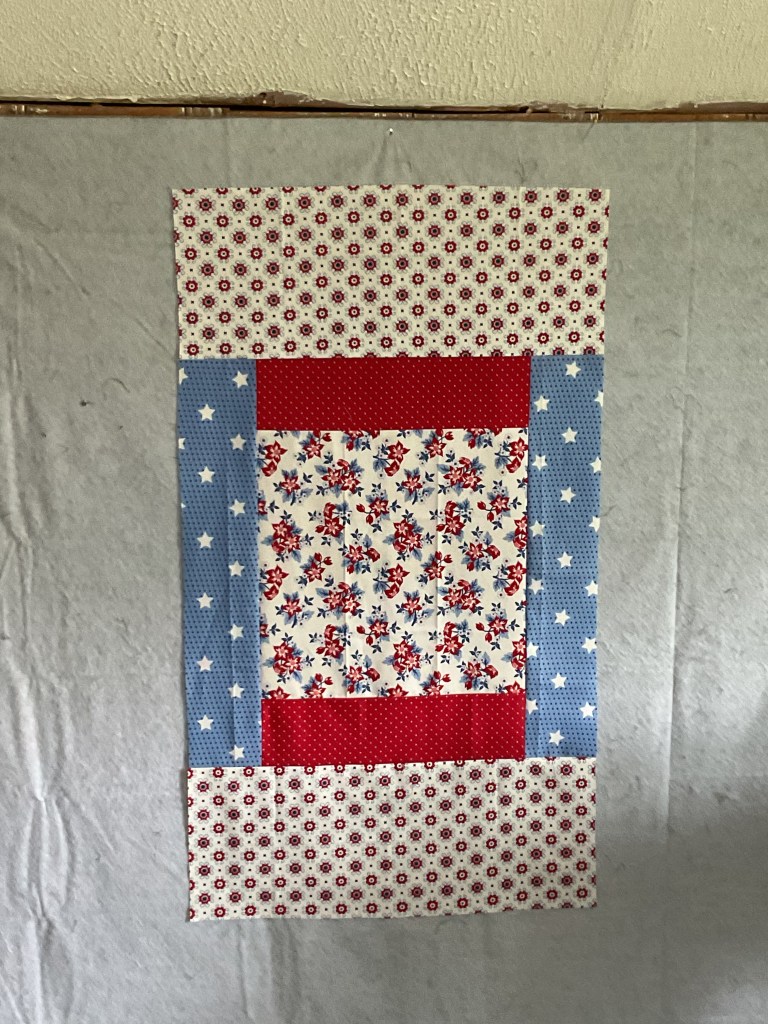 A patchwork quilt design featuring red, white, and blue fabrics with floral patterns and stars, arranged in a rectangular layout.