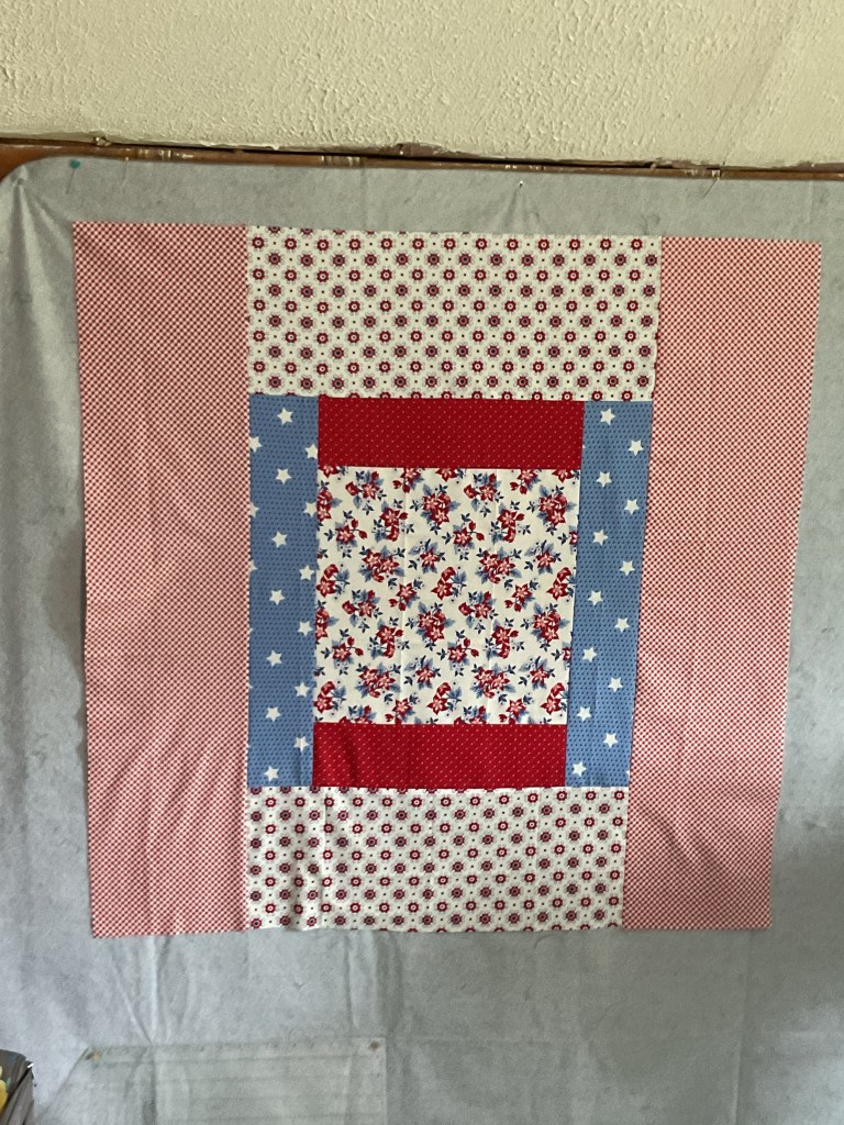 A colorful quilt block featuring a mix of red, white, and blue fabrics with various patterns including polka dots and floral designs.