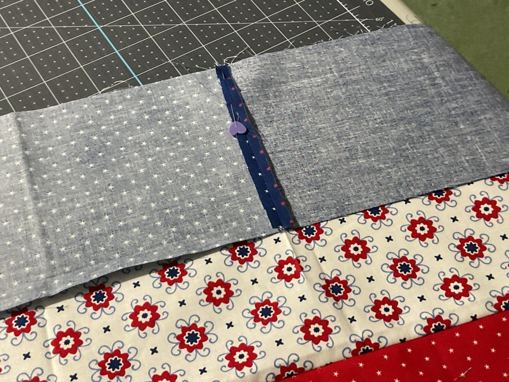 A close-up view of three fabric pieces, featuring a blue fabric with white stars, a solid blue patch, and a floral print in red and white, arranged on a cutting mat.