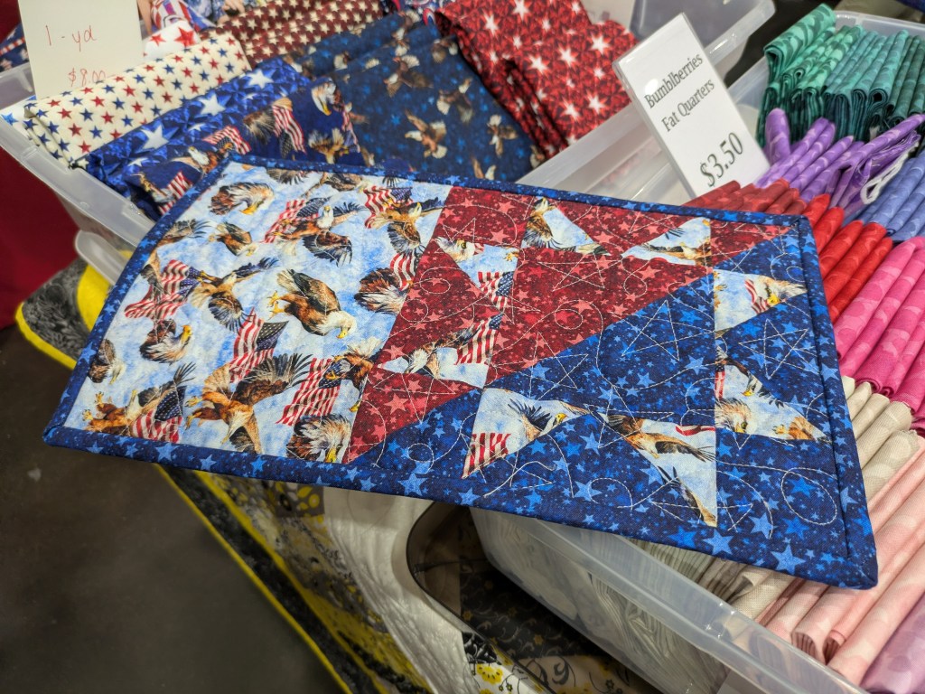 A colorful quilted table runner featuring a patriotic design with eagles, American flags, and stars in red, white, and blue fabric.