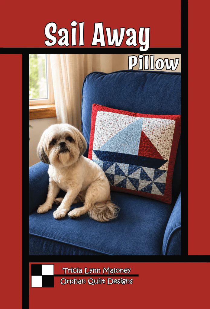 A small dog sitting on a blue sofa beside a decorative pillow featuring a sailboat and quilt patterns.