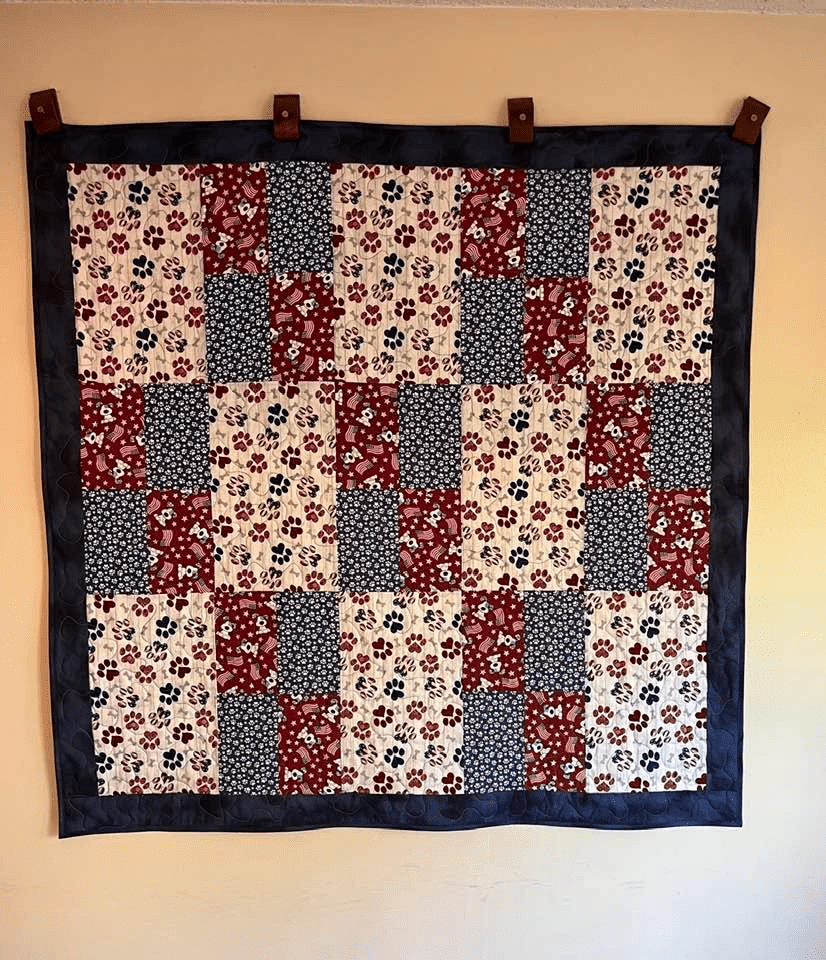 A colorful quilt hanging on a wall, featuring a patchwork design with red, navy blue, and floral patterns.