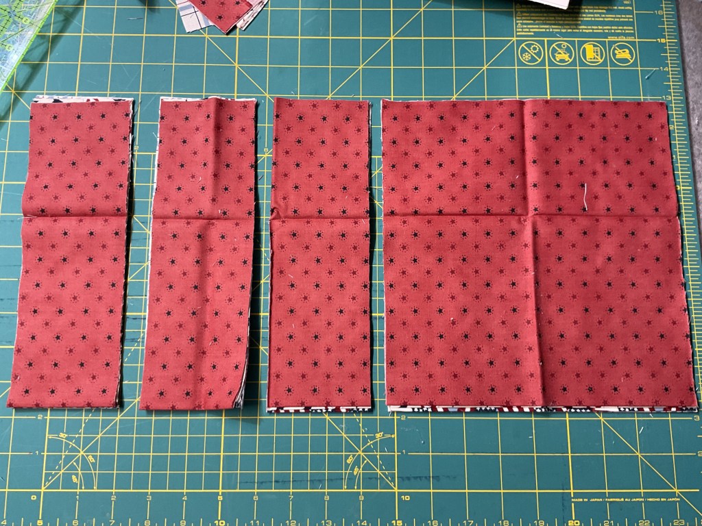 Four pieces of red fabric with a star pattern, arranged on a green cutting mat with grid lines.
