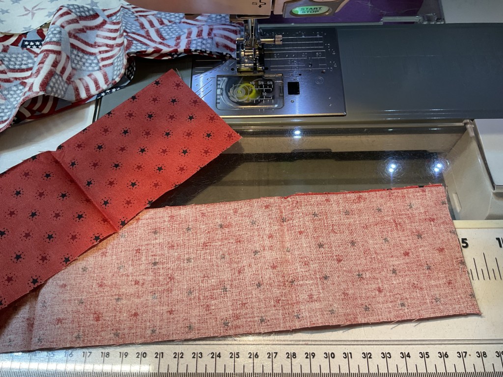 Close-up of a sewing machine with fabric pieces laid out, featuring red fabric with black stars and light reddish fabric with a subtle pattern.
