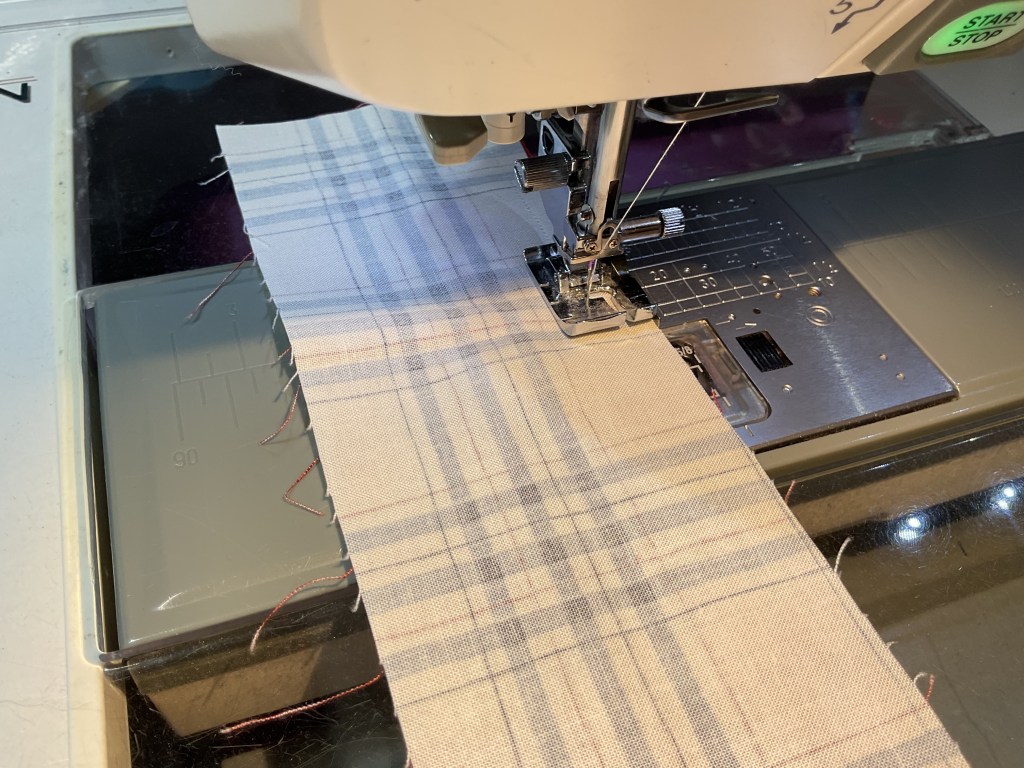 Close-up of a sewing machine with a piece of fabric being stitched, featuring a plaid pattern.