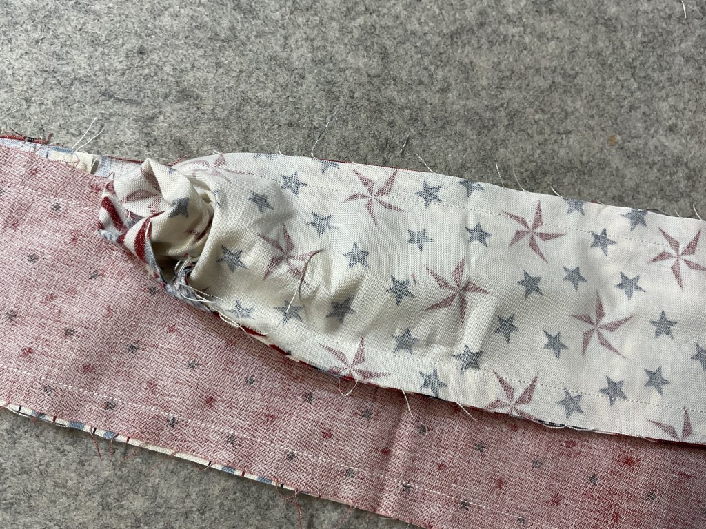 Close-up of two pieces of fabric: one patterned with red and blue stars on a cream background, the other in a solid red with small speckles, partially sewn together.