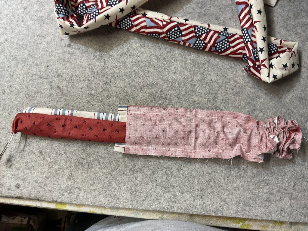 A fabric-covered sword or sword-like object lying on a gray surface, surrounded by additional fabric pieces featuring patriotic patterns.