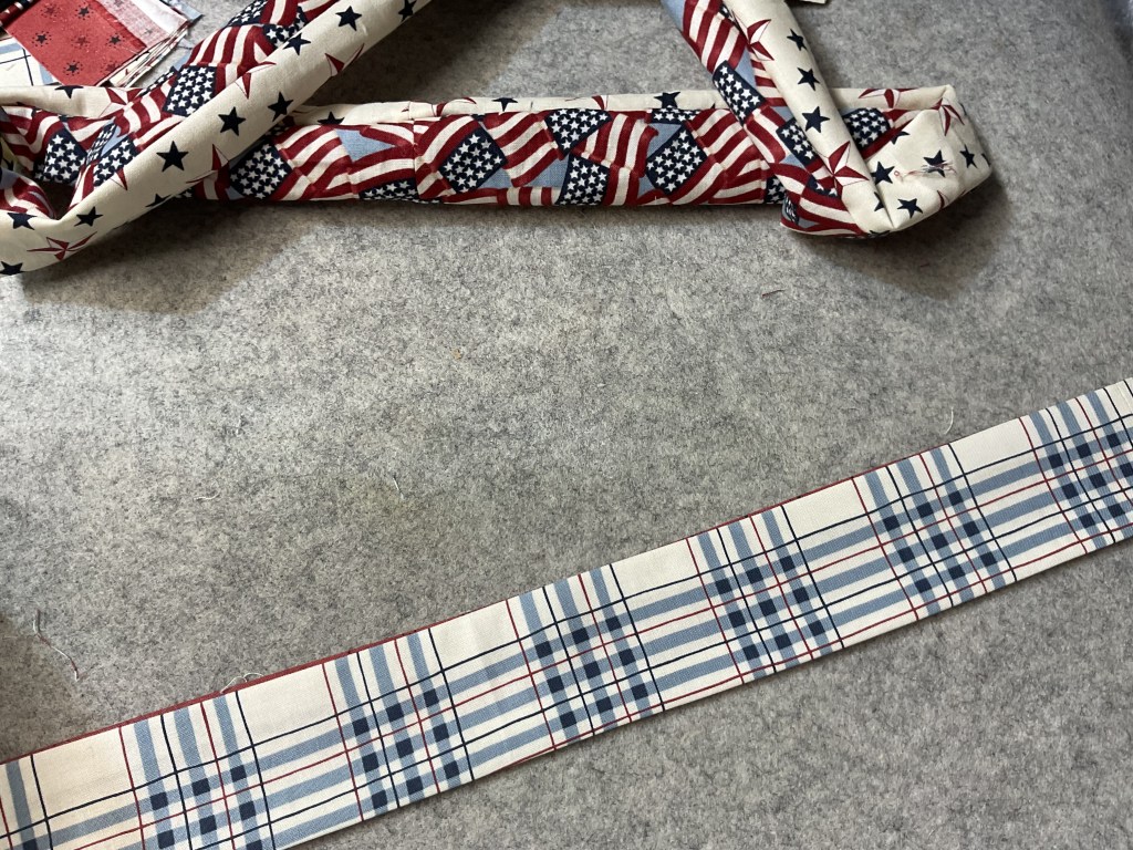 A close-up view of fabric strips featuring red, white, and blue patterns, including American flags and a plaid design, laid out on a gray felt surface.