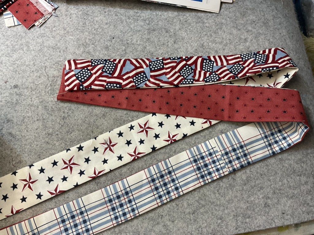 Three fabric strips featuring patriotic patterns, including American flags, stars, and plaid designs, laid on a textured background.