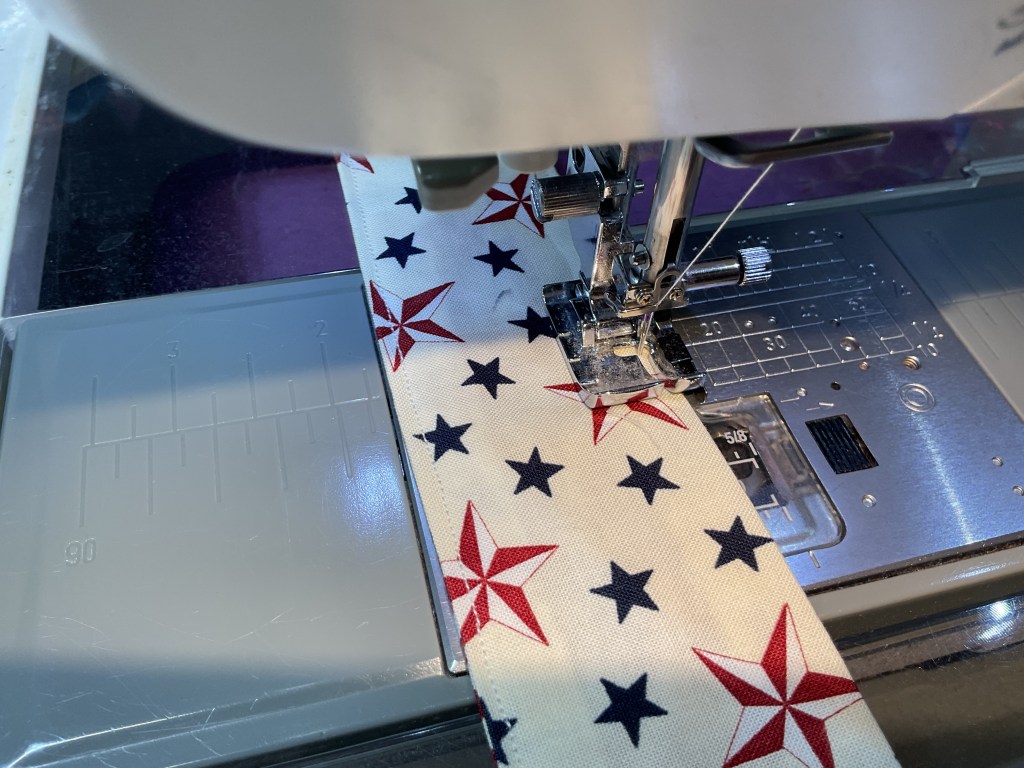 Close-up of a sewing machine stitching a fabric strip decorated with red stars and blue patterns.