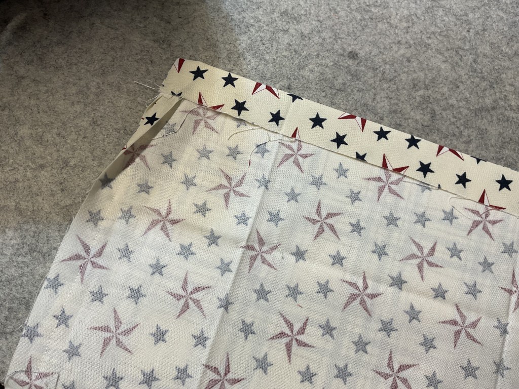 Two pieces of fabric with star patterns, one in red, white, and blue, and another in gray and red stars on a white background, laid on a gray surface.