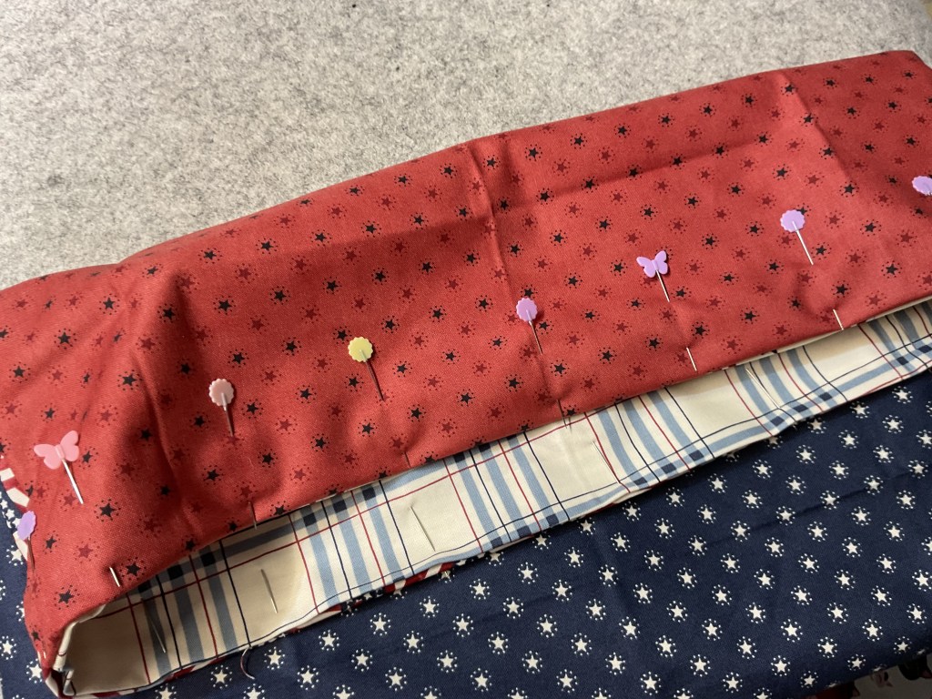 A piece of red fabric with a pattern of stars and small flowers, pinned to a striped fabric and a blue patterned fabric underneath.