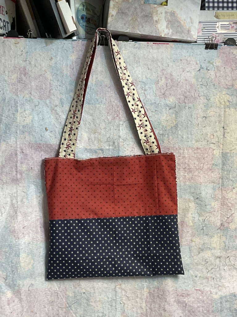 A handmade tote bag with a red top section featuring small polka dots, and a navy bottom section with white star patterns. The bag has patterned straps.