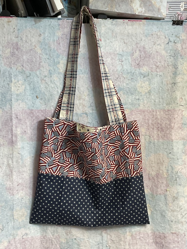 A fabric tote bag featuring a pattern of red and blue flags on top and a solid navy bottom with white polka dots.