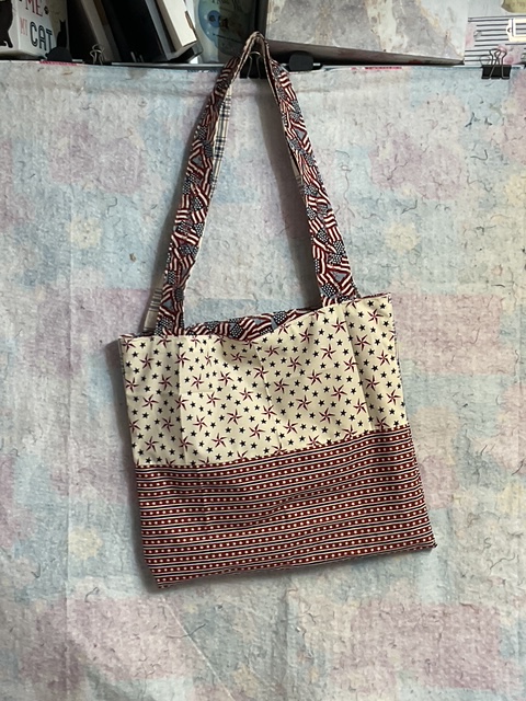 A tote bag with a star and stripe pattern, featuring a solid red striped bottom and handles.