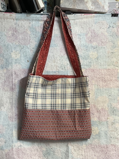 A plaid and polka dot fabric tote bag hanging against a light-colored backdrop.