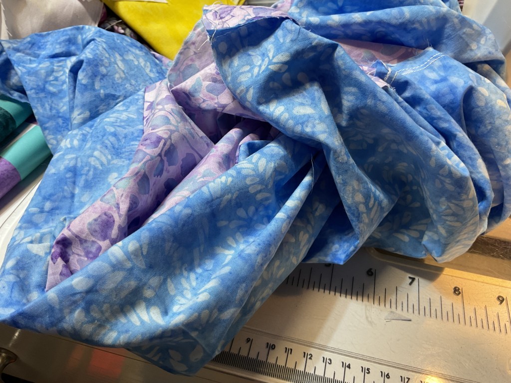 A collection of colorful fabrics in shades of blue and purple, arranged in a crumpled manner on a sewing table.
