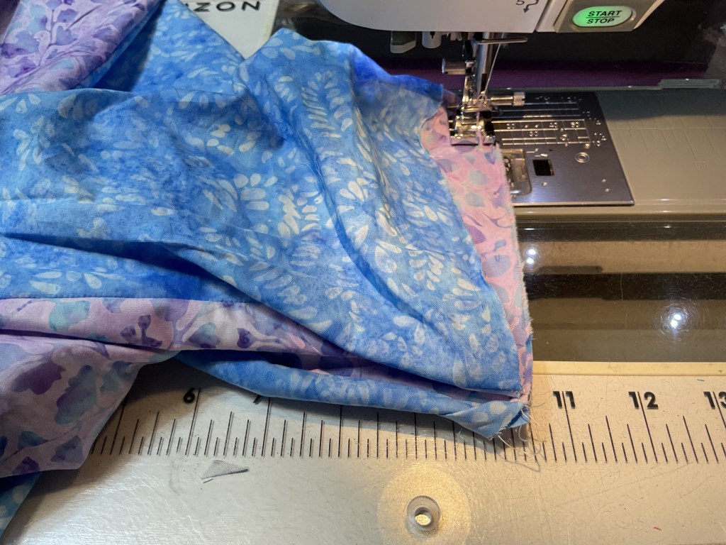 Close-up of a sewing machine with colorful fabric pieces being stitched together, showcasing a blue and purple floral pattern.