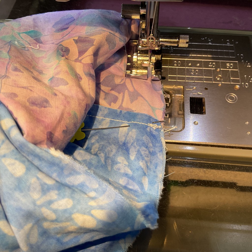 Close-up of a sewing machine stitching together two pieces of patterned fabric, featuring a pink and blue floral design.