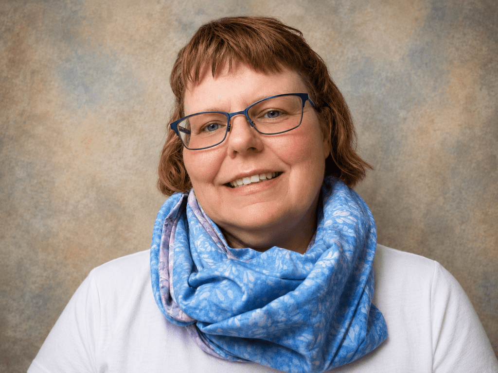 A smiling woman with short brown hair wearing glasses and a blue patterned scarf, against a textured background.