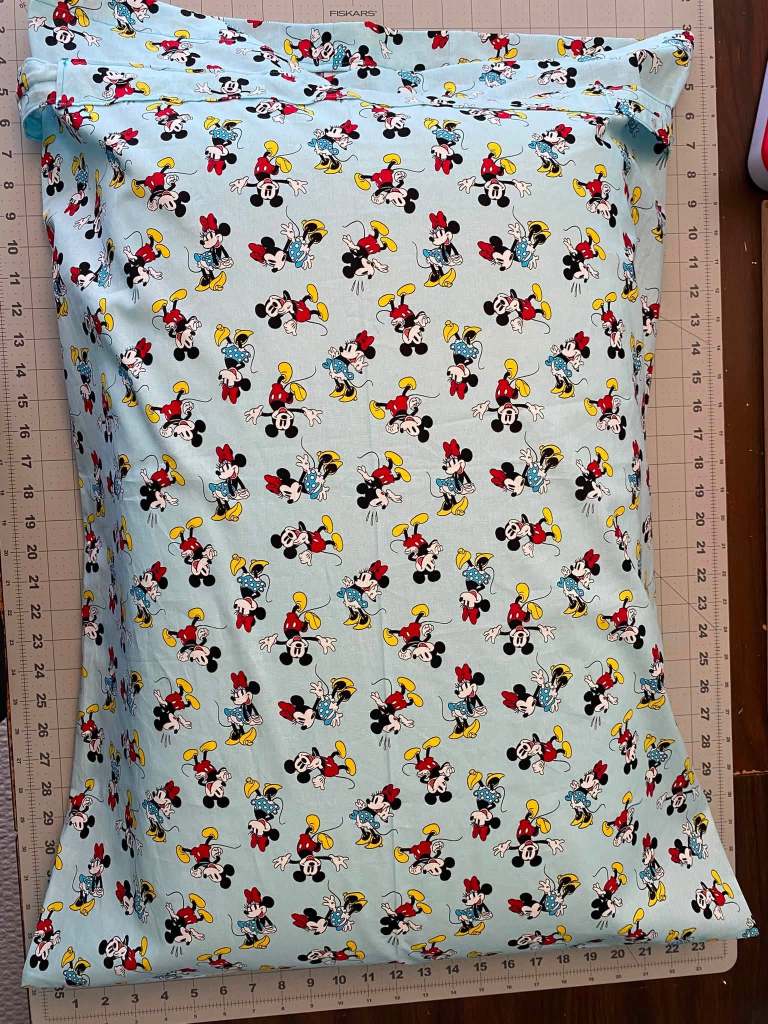 A pillowcase featuring a repeating pattern of Mickey and Minnie Mouse characters on a light blue background.