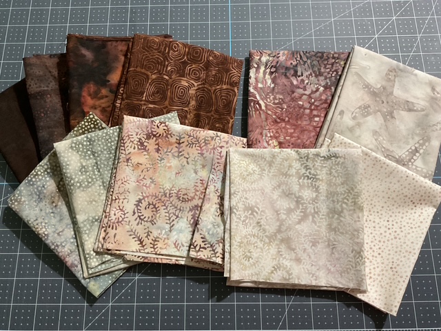 A collection of various patterned fabric squares arranged on a cutting mat, featuring earthy tones and intricate designs.