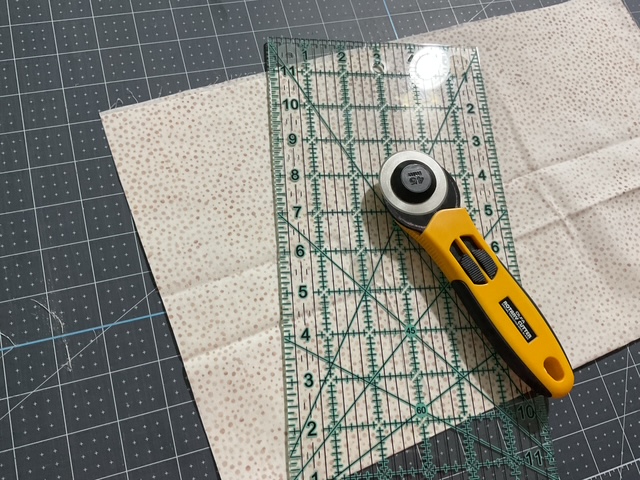 A rotary cutter and a clear quilting ruler placed on a patterned fabric on a cutting mat.