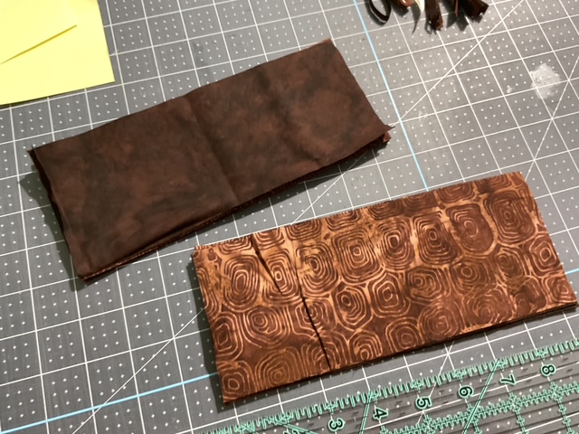 Two pieces of patterned fabric on a cutting mat, one solid brown and one with an intricate circular design.