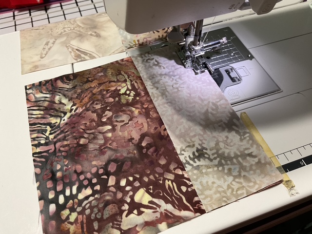 A close-up view of a sewing machine stitching together pieces of fabric with intricate patterns, featuring a mix of earthy colors and textures.