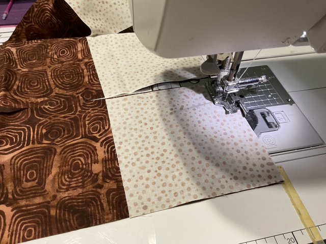 Close-up of a sewing machine stitching two pieces of patterned fabric together, featuring a brown swirly design and a light-colored polka dot pattern.