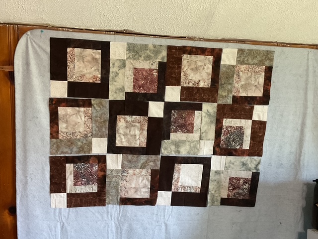 A patchwork quilt layout featuring various brown and cream square blocks arranged in a grid pattern against a gray backdrop.