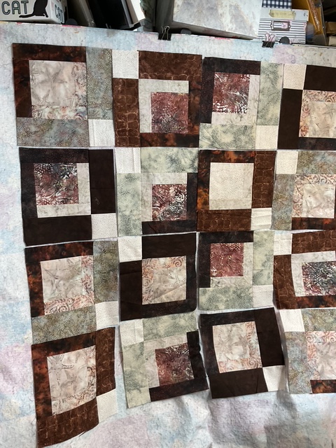 A patchwork quilt featuring a grid design composed of various fabric squares in earthy tones, including browns, greens, and creams.