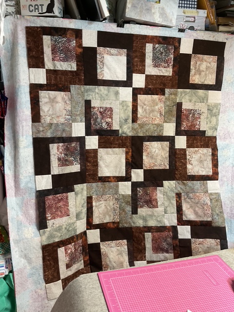 Quilt display featuring a geometric pattern of alternating square blocks in browns, creams, and earthy tones.