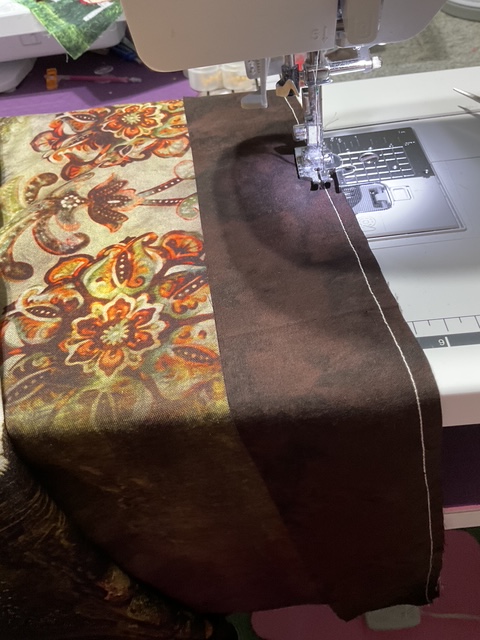 Close-up of a sewing machine stitching colorful fabric with a floral pattern alongside a solid brown fabric.