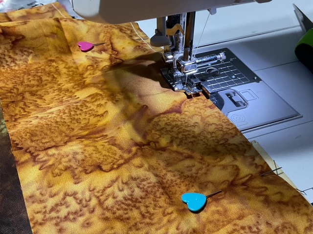 Close-up of a sewing machine and a piece of fabric with heart-shaped pins attached, showcasing a vibrant brown pattern.