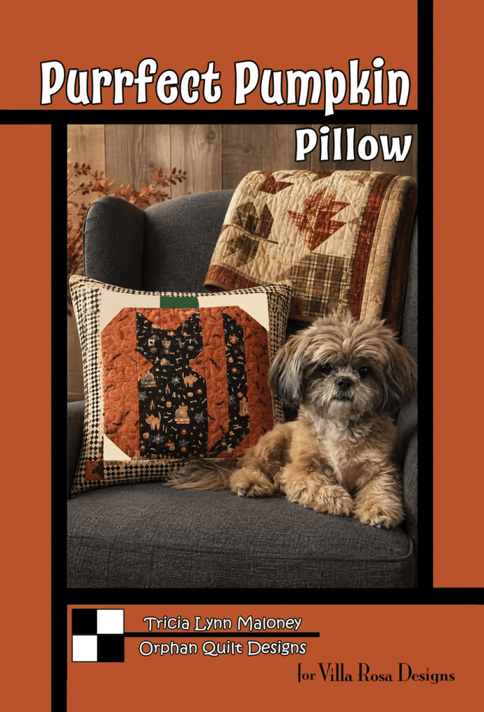 A cozy scene featuring a small dog sitting beside a decorative pillow with a pumpkin design on a gray couch. A quilt with autumn leaves is draped over the back of the couch.