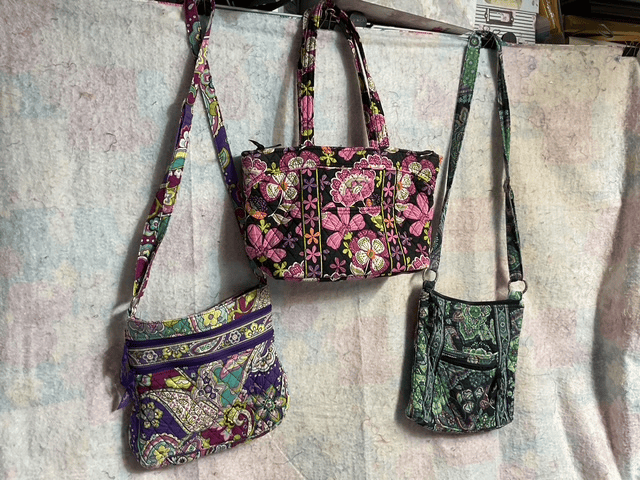Three colorful fabric bags displayed against a textured background. The bags feature floral patterns and various styles, including a larger handbag with short handles and two smaller crossbody bags.