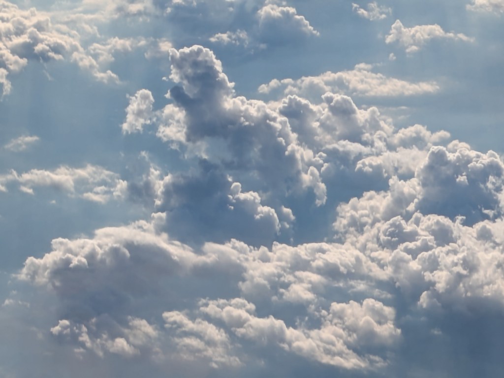 A view of fluffy white clouds scattered against a blue sky, with soft sunlight illuminating the scene.