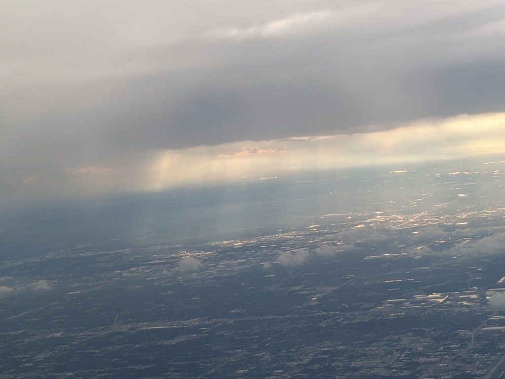 Aerial view of a landscape featuring clouds and sunlight rays breaking through gray skies.