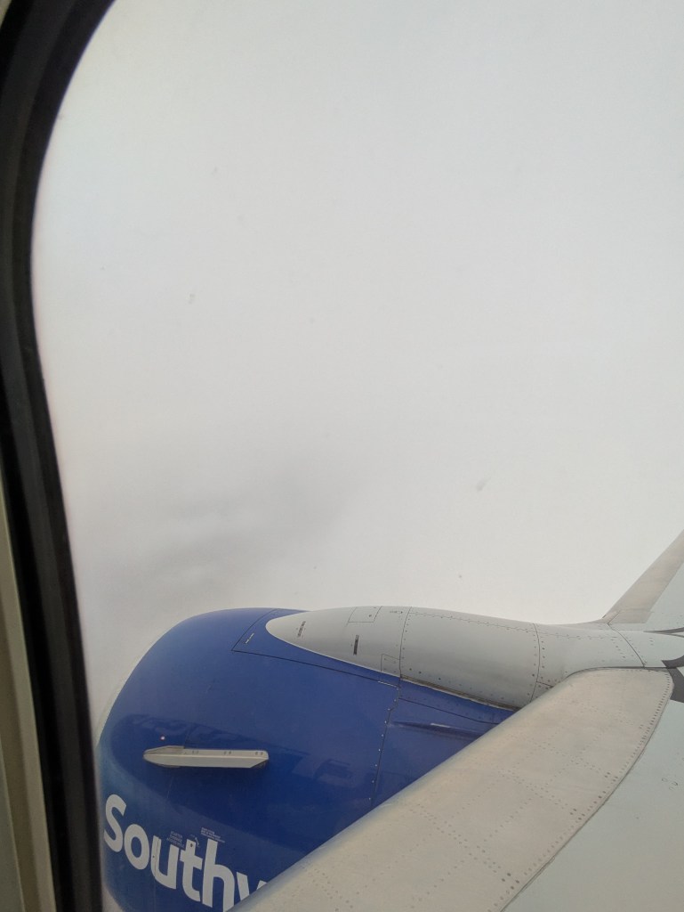 View from an airplane window showing the wing and engine of a Southwest Airlines plane over a cloudy sky.