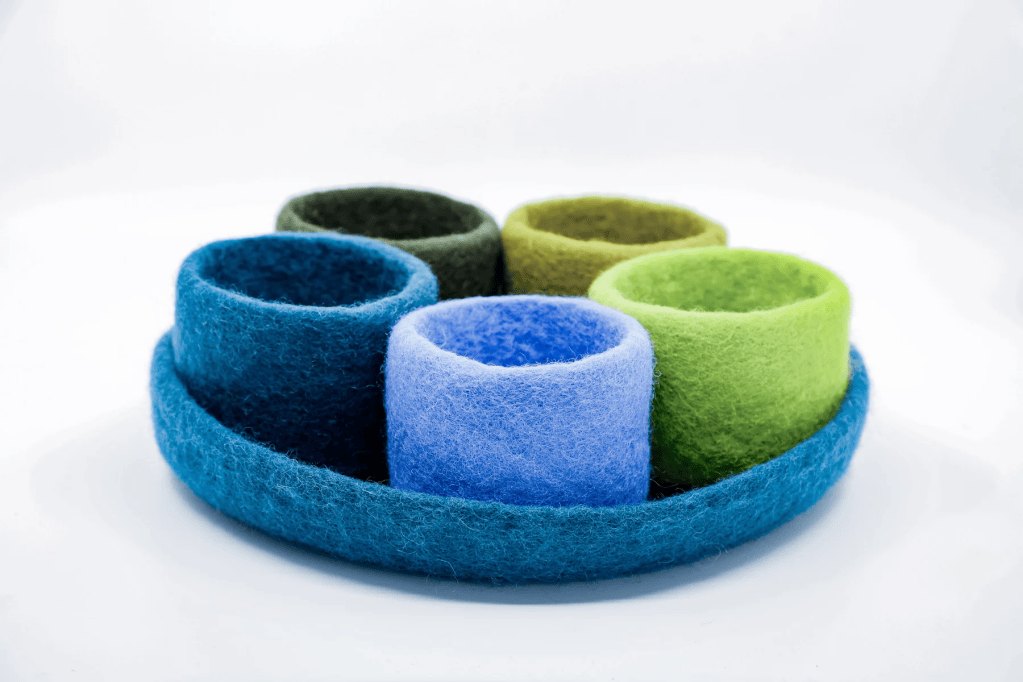 A set of five colorful felt containers arranged on a circular base, featuring shades of blue, green, and purple.