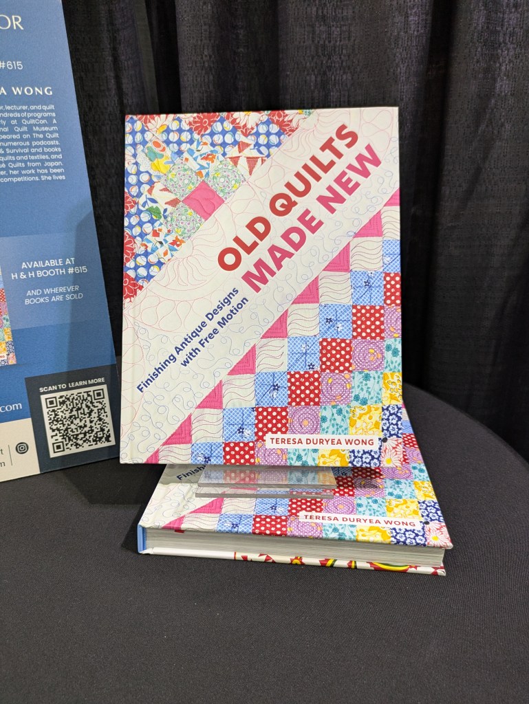 A close-up view of the book 'Old Quilts Made New' by Teresa Duryea Wong, featuring colorful quilt patterns on the cover, placed on a dark surface with a QR code partially visible.